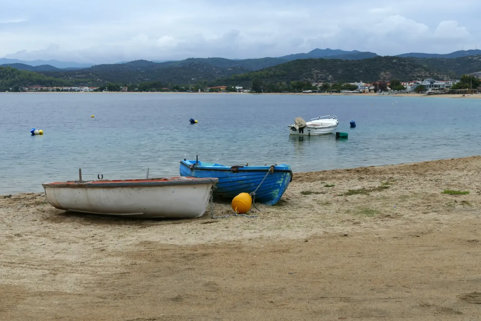 Δύο βάρκες τραβηγμένες στην άμμο της Τορώνης, με τα βουνά της Σιθωνίας πίσω